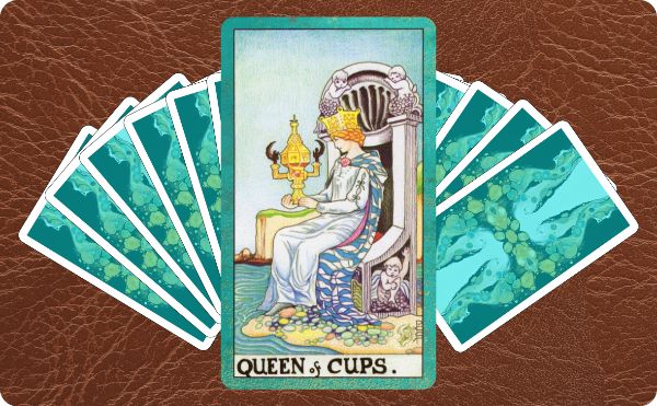 Rider Waite depiction of the Queen of Cups tarot card sitting on top of a spread of several other tarot cards.