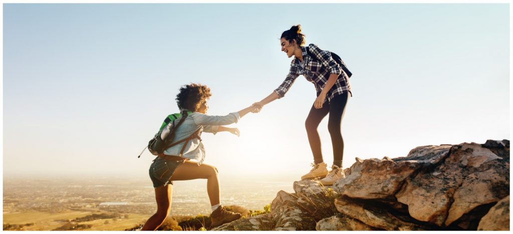 Person on a rocky mountain helping another person up the mountain.